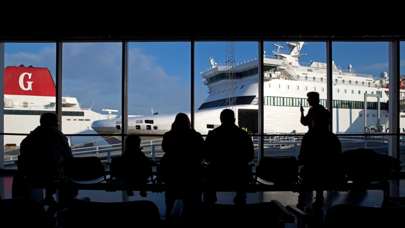 En grupp människor som står framför ett fönster med fartyg i bakgrunden.