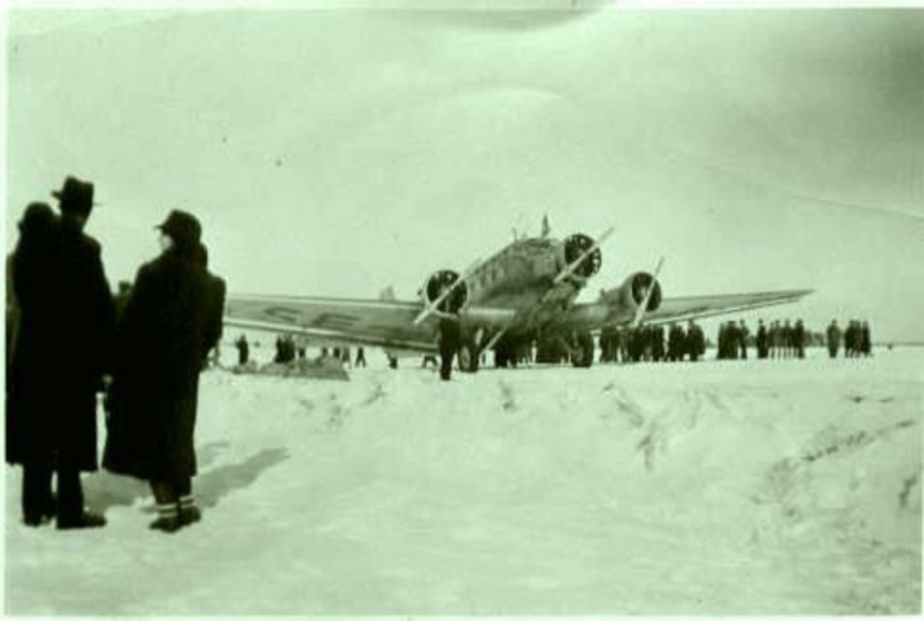 Äldre foto med personer som står framför ett flygplan från andra världskriget.
