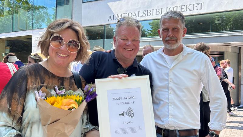 Tre glada personer visar upp diplom och blommor.