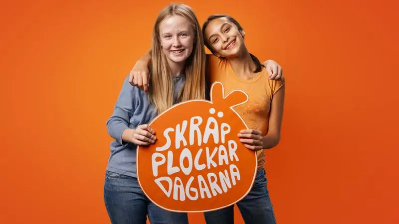 Två unga tjejer håller om varandra och håller i en skylt med texten Skräpplockardagarna.
