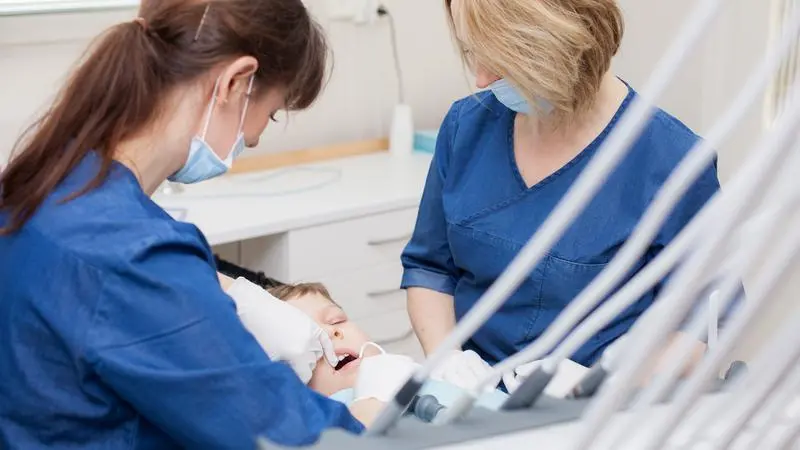 Tandvårdspersonal i blå arbetskläder tar hand om patient.