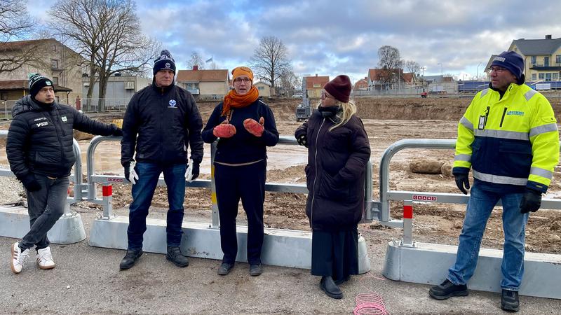 Fem personer som står framför en avspärrad byggarbetsplats