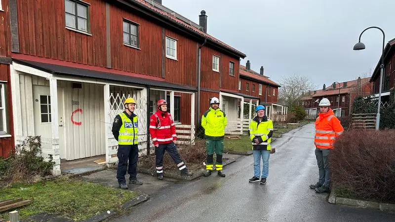 Blåsjuspersonal står framför röda radhuslängor i trä. 