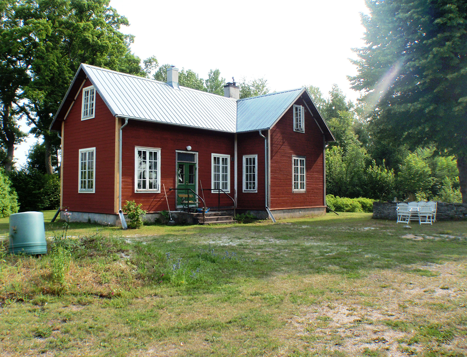 Ett rött hus med träfasad, vita fönster, en grön ytterdörr och ett plåttak.