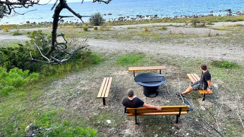 Två personer sitter vid en grillplats med bänkar vid havet
