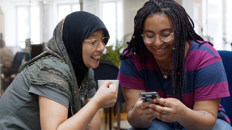 Två kvinnor sitter och tittar på en telefon