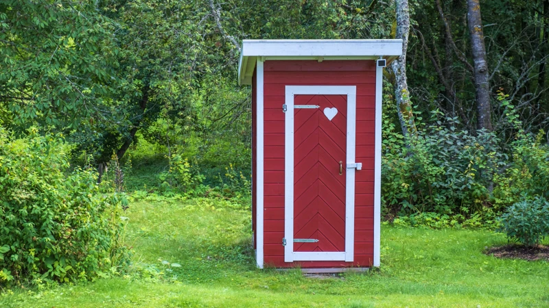 Ett litet rött utedass mitt i en skog.