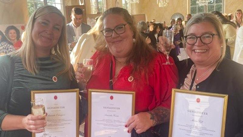 Tre kvinnor som håller i varsitt inramat diplom och champagneglas