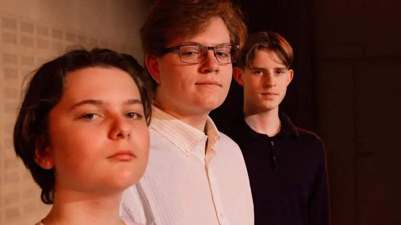 Tre unga personer står på rad och ser in i kameran.