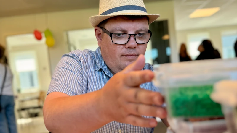 En man i hatt och glasögon tittar på en behållare.