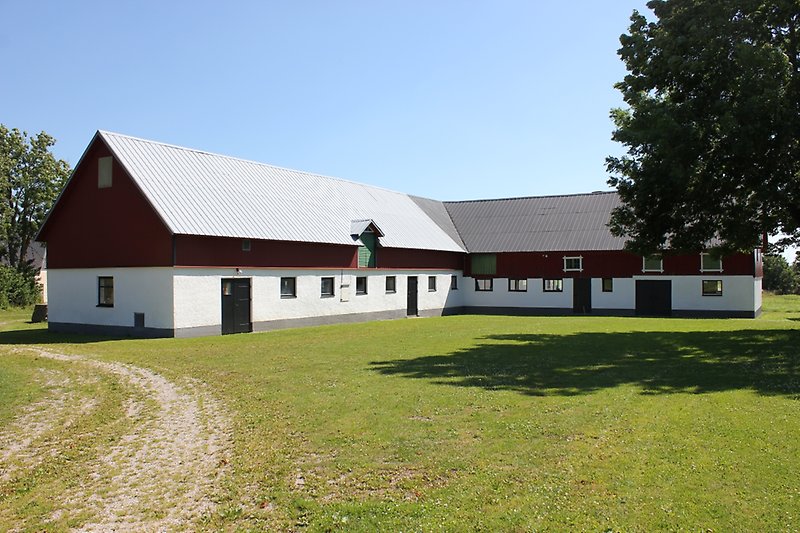 En rödvit lada med svarta dörrar, svarta fönster och ett grått plåttak.