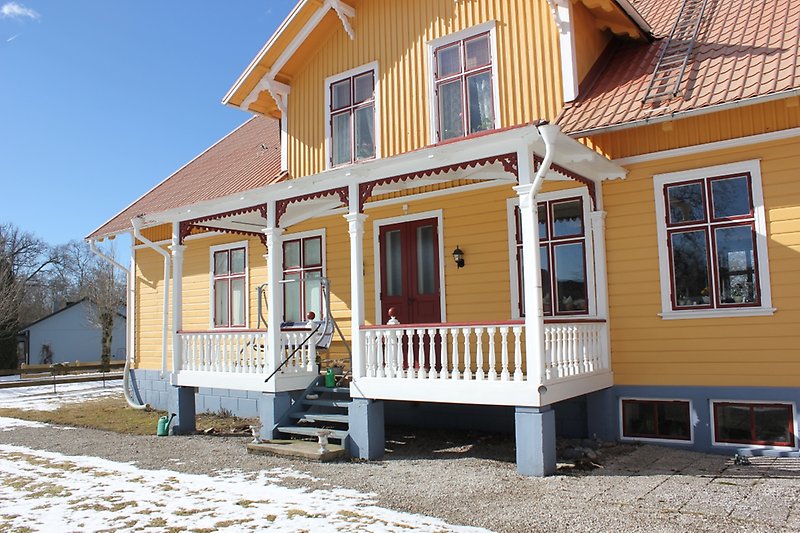 Ett gult hus med en träfasad, röda fönster och ett rött tak.