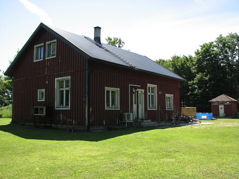 En svart stuga med vita fönster och ett svart plåttak.