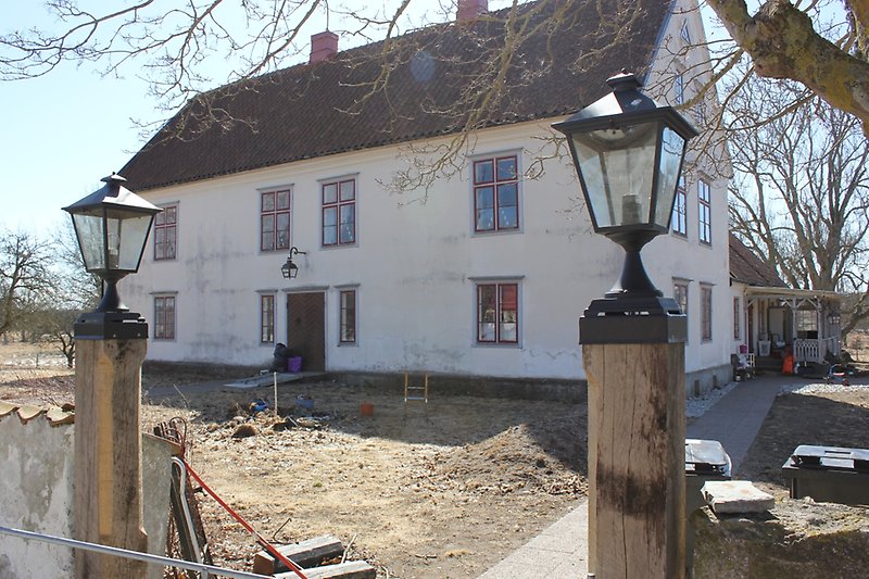 Ett vitt hus bestående av två våningar med röda fönster och ett brunt tegeltak med två röda skorstenar.