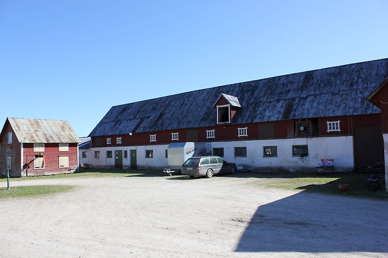 Rödvit ladugård med vita fönster på övre våningen och gröna fönster på den nedre våningen, samt gröna dörrar och ett rostigt plåttak.