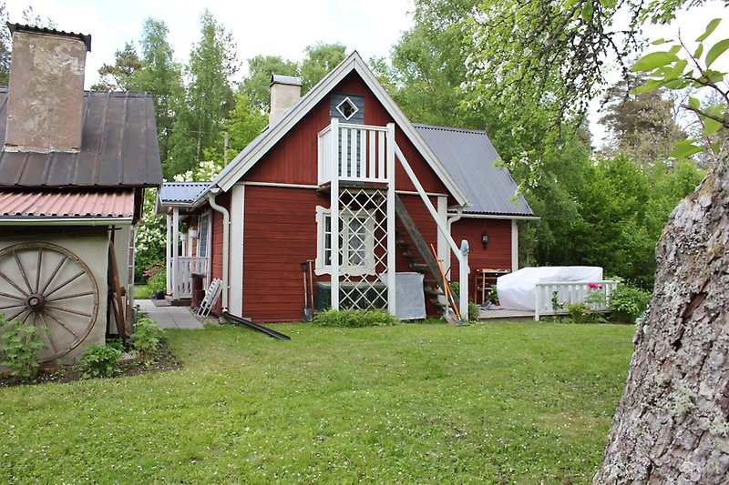 En röd stuga med vita detaljer, vita fönster och ett plåttak.