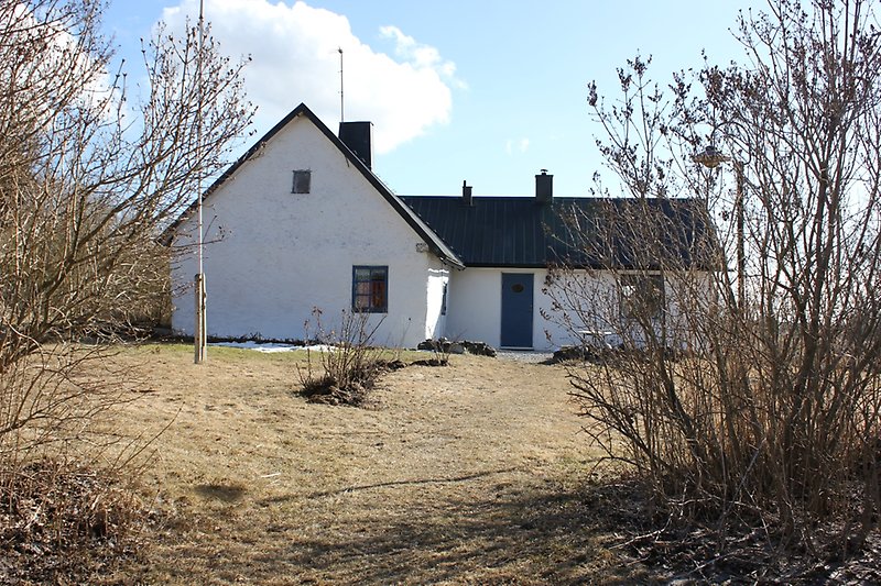 Ett vitt hus med blåa fönster, en blå ytterdörr och ett svart plåttak.