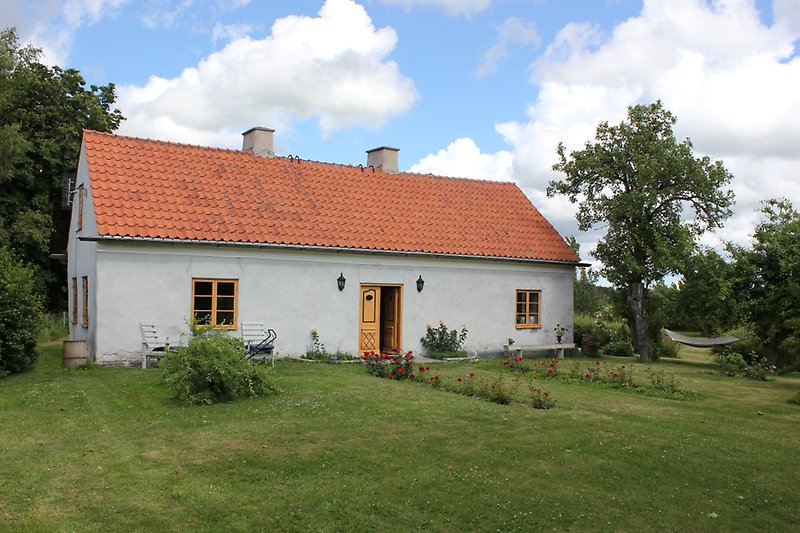 Envånings hus med ett rött tak, två skorstenar och bruna fönster.