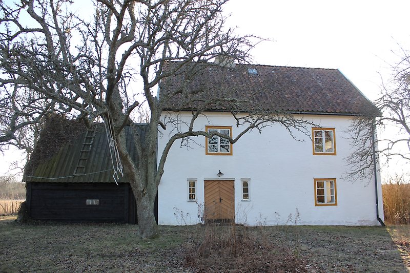 Ett vitt hus med gula fönsterramar, vita fönster, gul ytterdörr och en svart tillbyggnad.