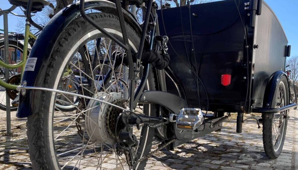 Svart ellastcykel med ett hänglås på vid en cykelparkering