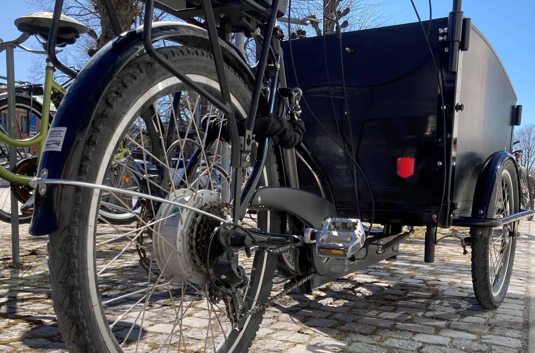 Svart ellastcykel med ett hänglås på vid en cykelparkering