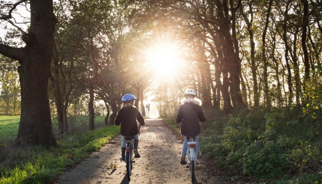 Två barn cyklar mot solen på en grusväg