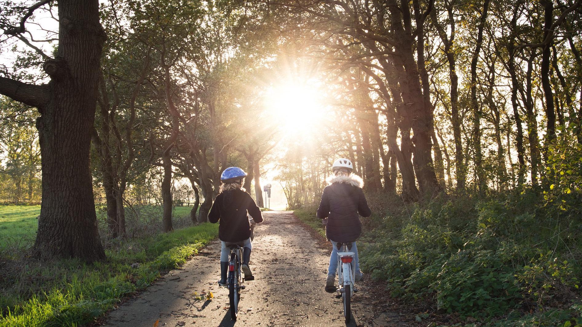 Två barn cyklar mot solen på en grusväg