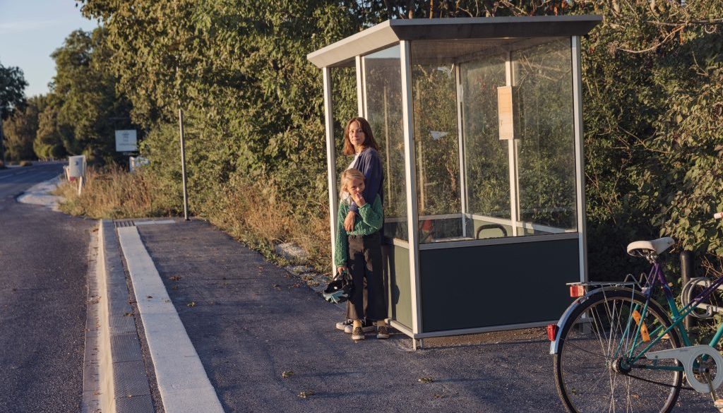 kvinna och barn står i busskur vid landsväg