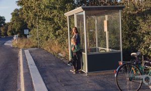 kvinna och barn står i busskur vid landsväg