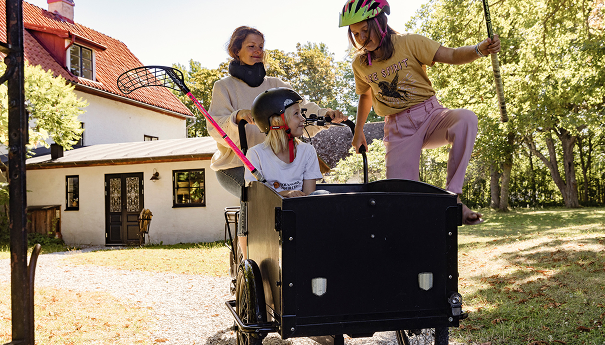 Kvinna cyklar lastcykel med två barn på en gårdsplan