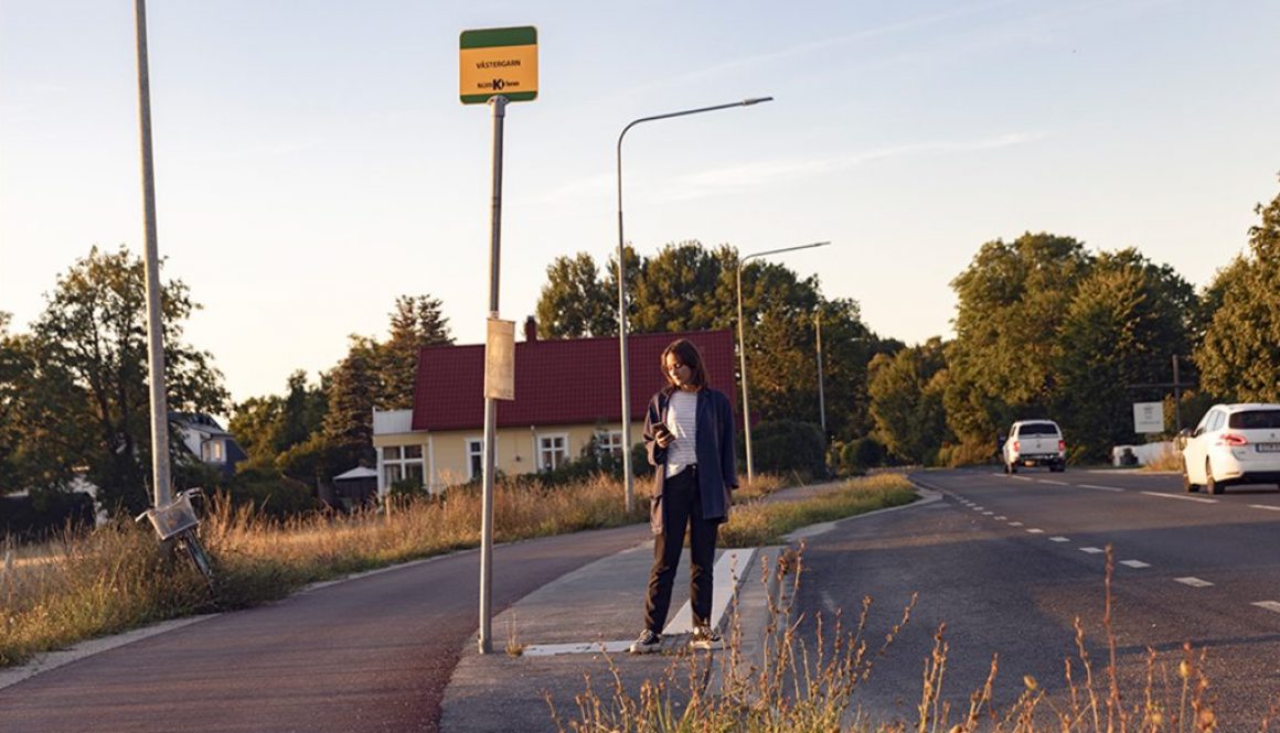 Kvinna väntar på bussen vid landsväg och tittar på sin mobiltelefon