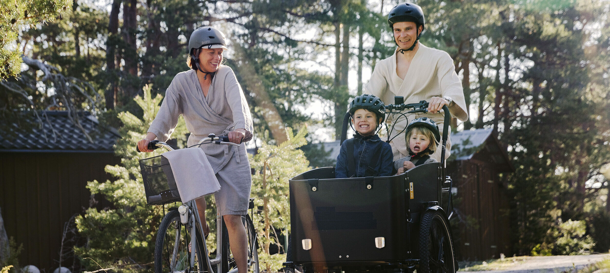 Två vuxna som cyklar och två barn som åker i ellastcykelns låda