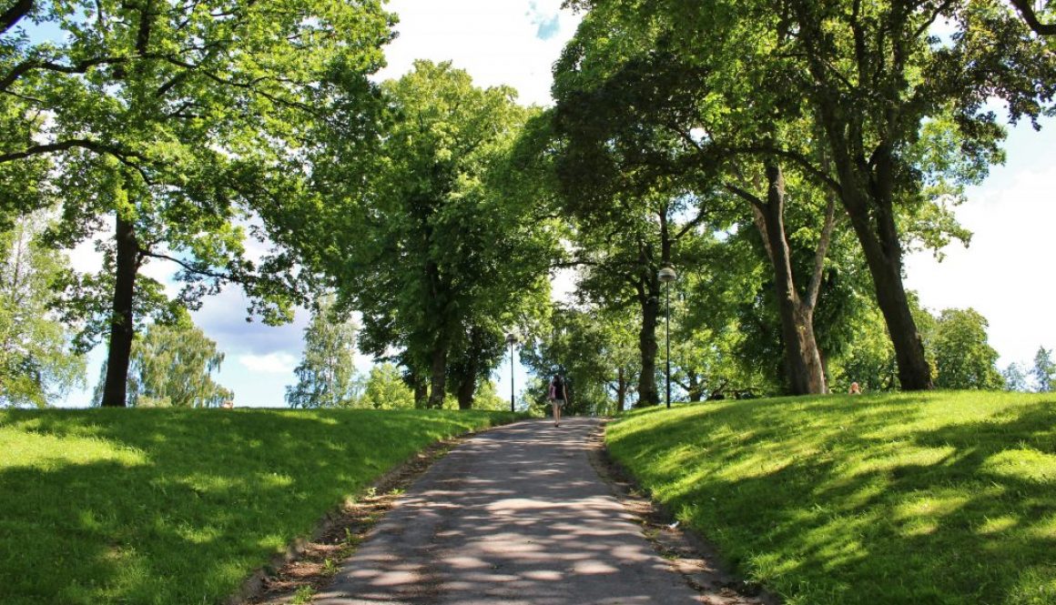 Kvinna som går uppför en parkväg omgiven av träd