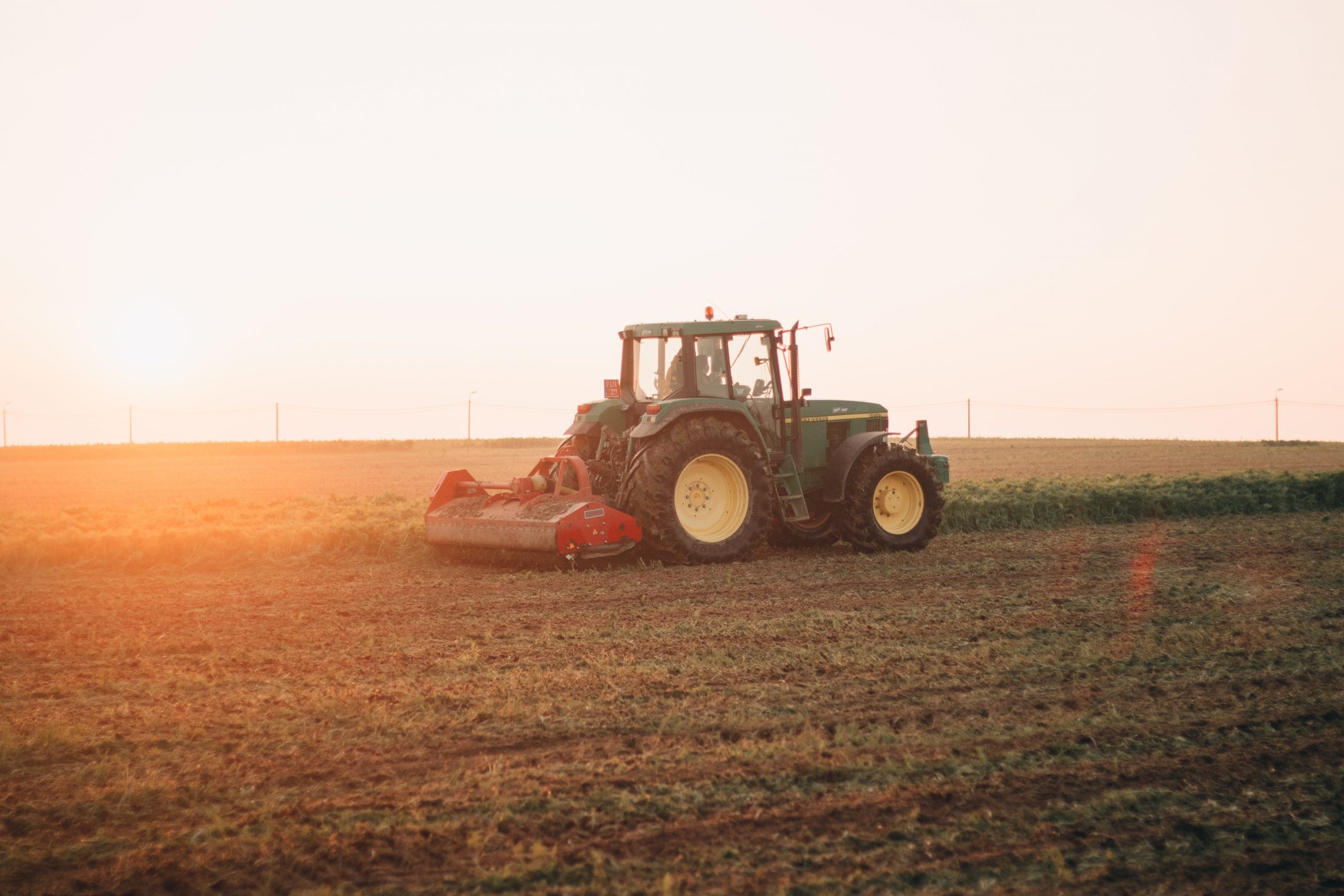 John Deere traktor kör maskin på fält i motljus