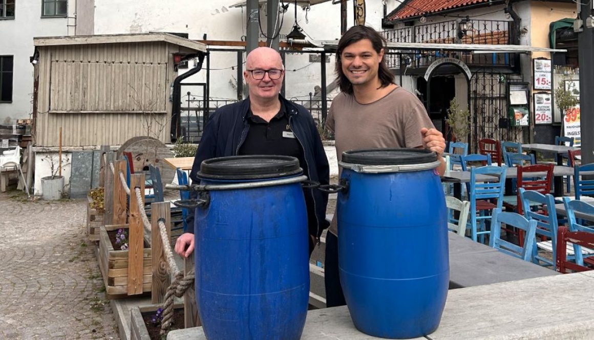 Två män framför två blåa 100l tunnor på en uteservering.