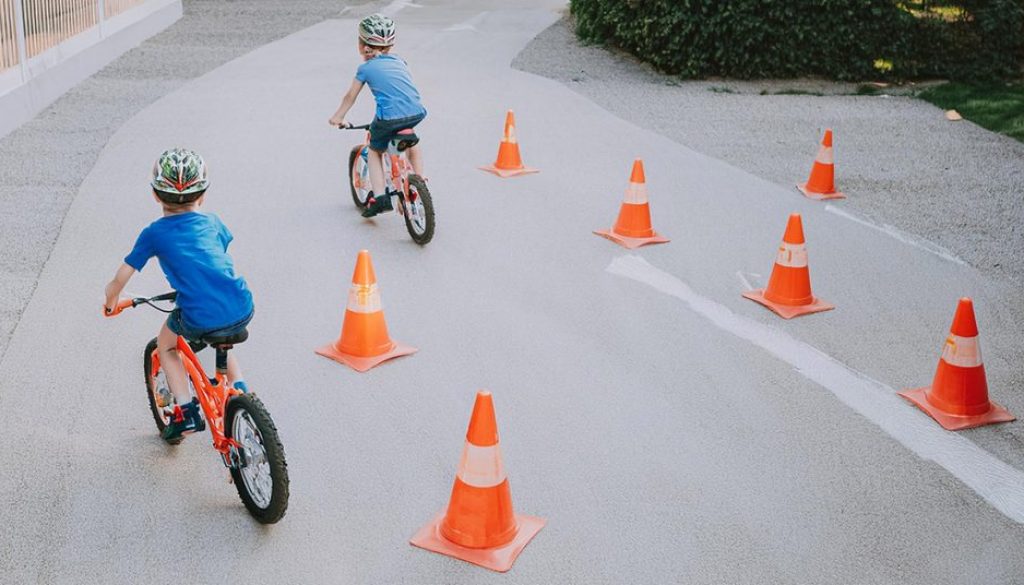 Två barn cyklar runt orangea koner på en asfalterad väg