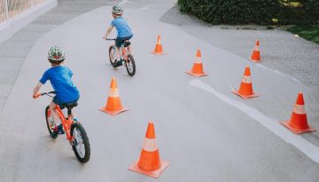 cykel_bana Två barn cyklar runt orangea koner på en asfalterad väg