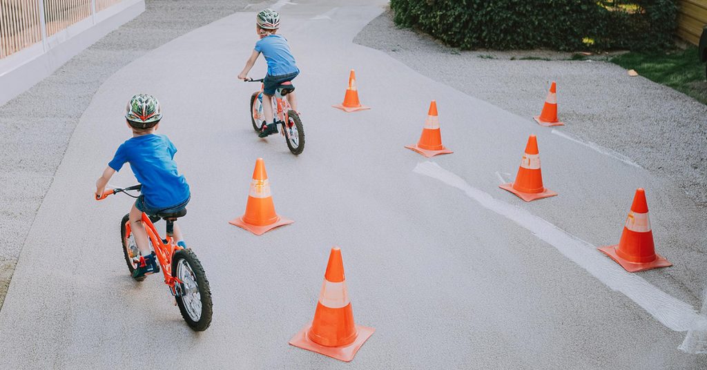 Två barn cyklar runt orangea koner på en asfalterad väg