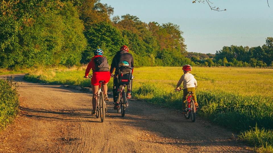 Familj cyklar på grusväg bredvid grön äng