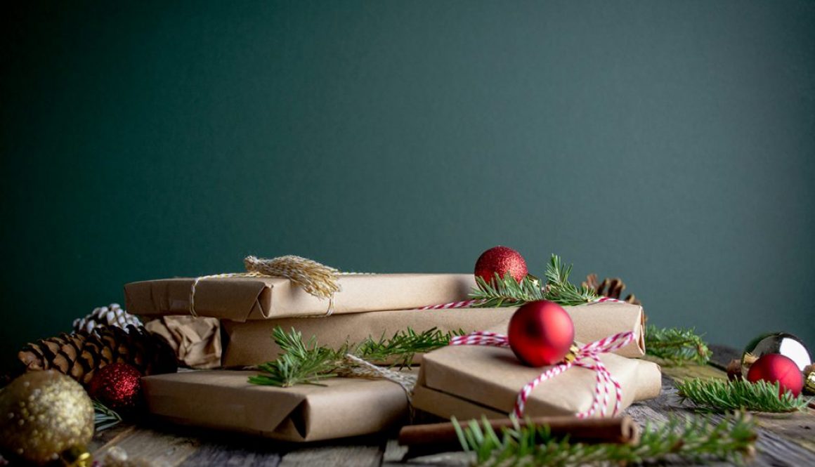 en hög med julklappar med brunt omslagspapper på ett träbord, röda julkulor och smågrankvistar